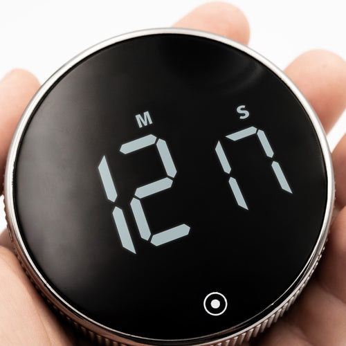 New Nordic Time fokusur holdt i hånden, der viser det digitale display og fremhæver urets kompakte størrelse og elegante design med tekstureret ramme.