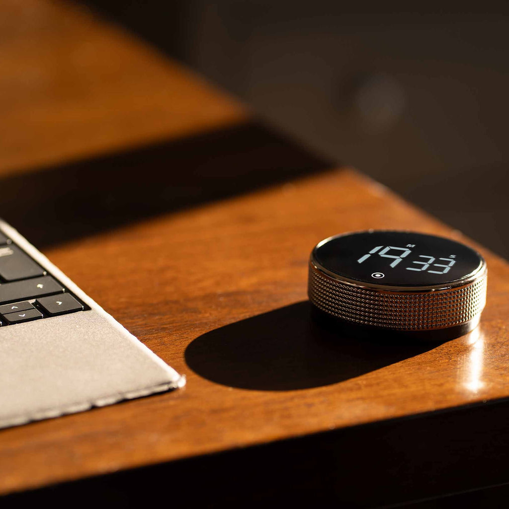 New Nordic Time fokusur placeret på et træbord ved siden af en bærbar computer, der fremhæver urets moderne design og funktionalitet i et stilfuldt arbejdsmiljø.