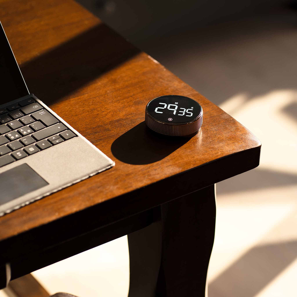 New Nordic Time fokusur placeret på et træbord ved siden af en bærbar computer, der viser urets moderne design og dets integration i et stilfuldt arbejdsmiljø.