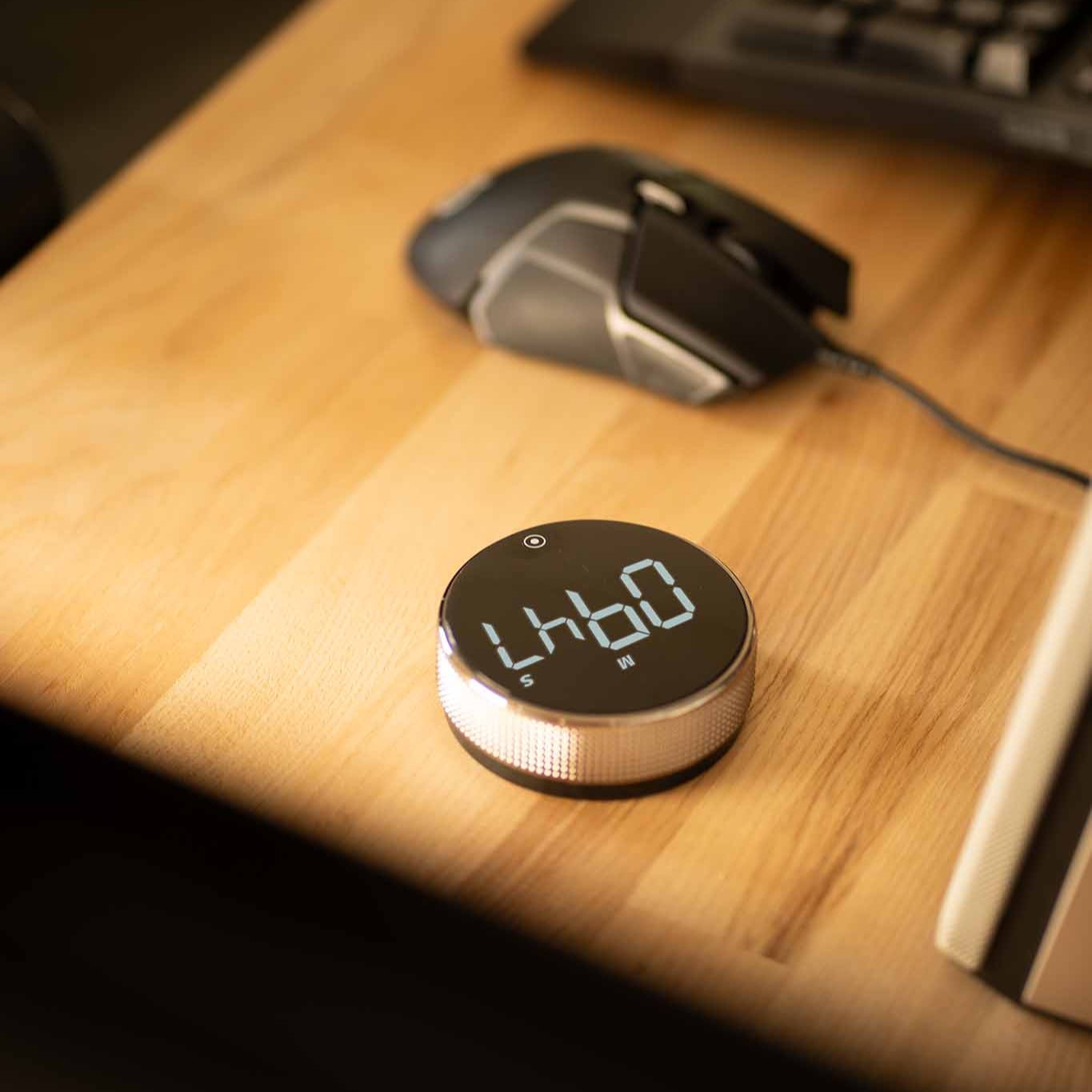 New Nordic Time fokusur placeret på et træbord ved siden af en computer-mus, der viser urets moderne design og brugervenlighed i et kontormiljø.